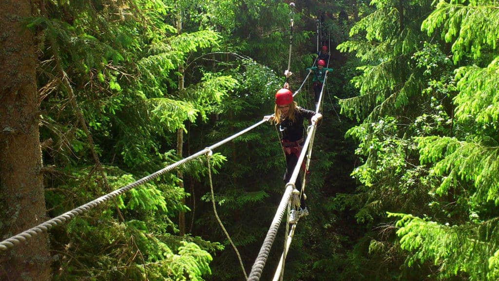 Some people walk across a burma bridge/ rope bridge.