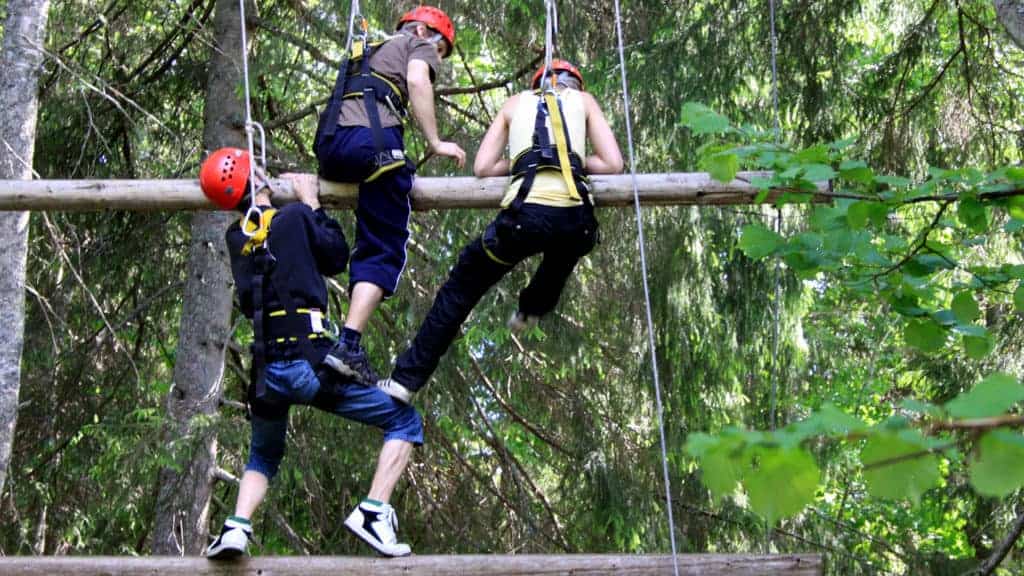 Three people climb a hell of a ladder with logs hanging in wires.