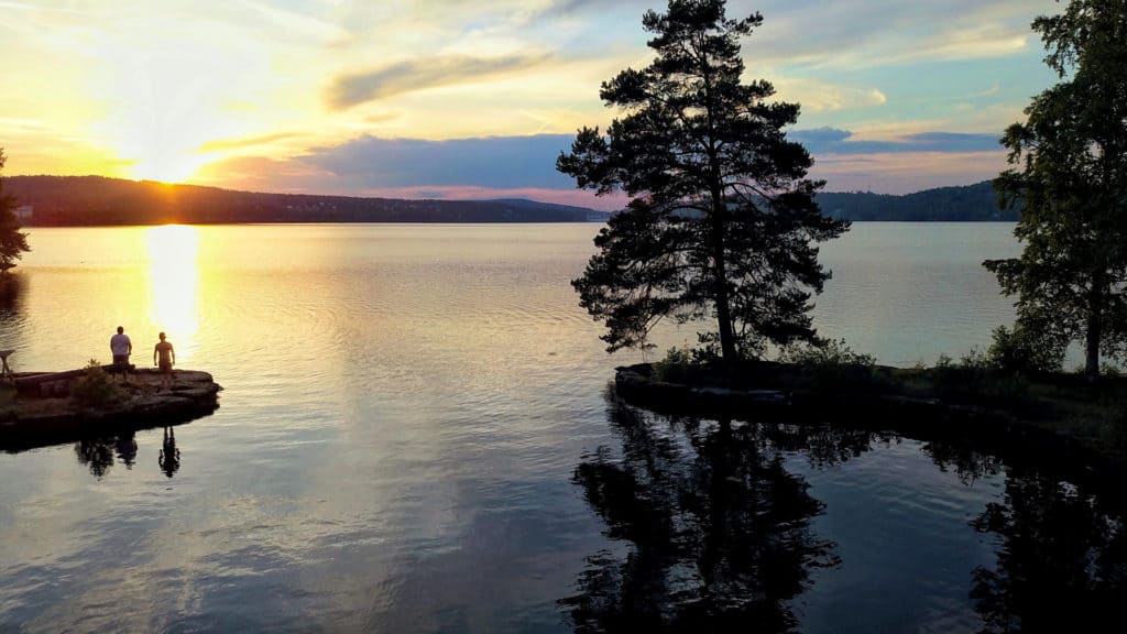 Two people stand on a promontory by a lake. It's a beautiful sunset.