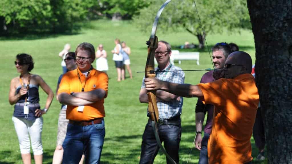 En man skjuter med pilbåge. Flera andra tittar på.