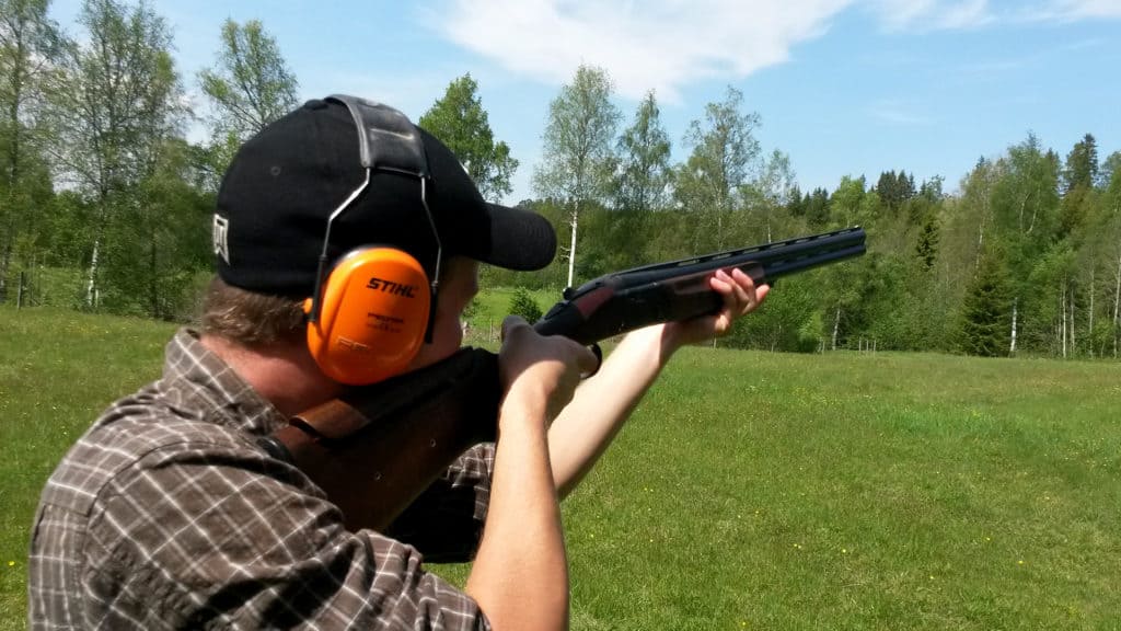 En man står med ett gevär och skjuter lerduva