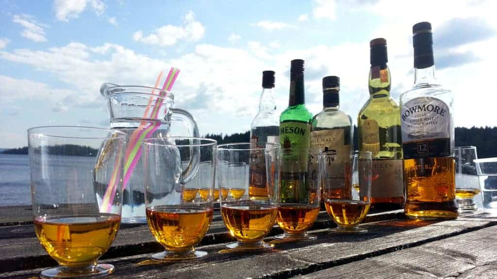 Whiskeyflaskor och glas står på ett bord. Sjön syns i bakgrunden.